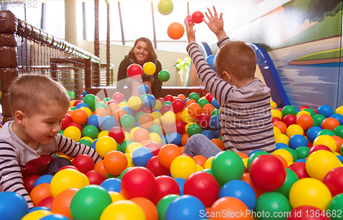 Image of young mom playing with kids in pool with colorful balls