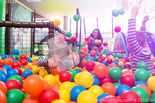 Image of young mom playing with kids in pool with colorful balls