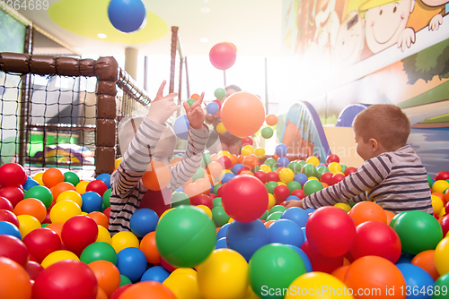 Image of young mom playing with kids in pool with colorful balls