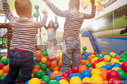 Image of young mom playing with kids in pool with colorful balls