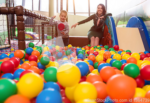 Image of young mom playing with kids in pool with colorful balls