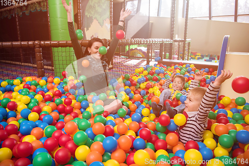 Image of young mom playing with kids in pool with colorful balls