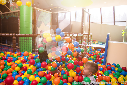 Image of young mom playing with kids in pool with colorful balls