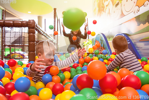 Image of young mom playing with kids in pool with colorful balls