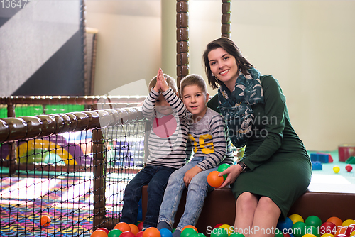 Image of young mom playing with kids in pool with colorful balls