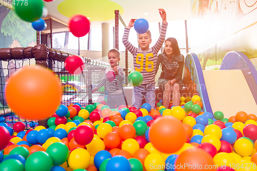 Image of young mom playing with kids in pool with colorful balls