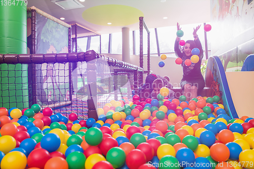 Image of young mom playing with kids in pool with colorful balls