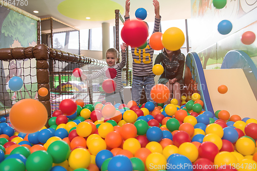 Image of young mom playing with kids in pool with colorful balls
