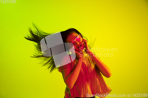 Image of Beautiful girl\'s facial expression in neon light on yellow studio background