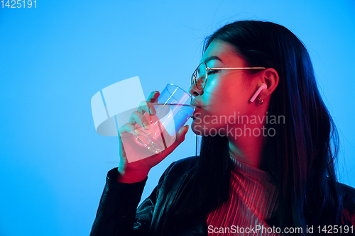 Image of Beautiful girl\'s facial expression in neon light on blue studio background