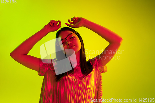 Image of Beautiful girl\'s facial expression in neon light on yellow studio background