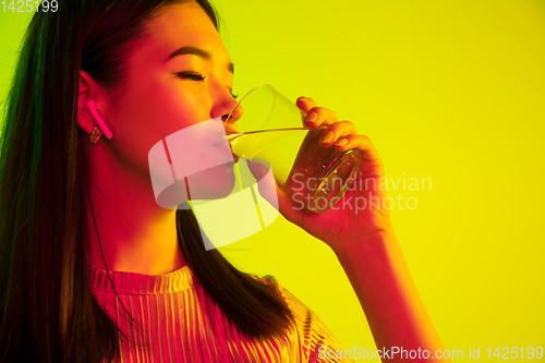 Image of Beautiful girl\'s facial expression in neon light on yellow studio background