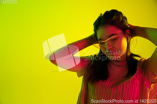 Image of Beautiful girl\'s facial expression in neon light on yellow studio background