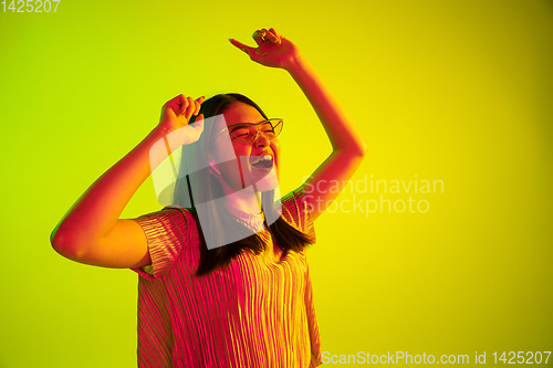 Image of Beautiful girl\'s facial expression in neon light on yellow studio background