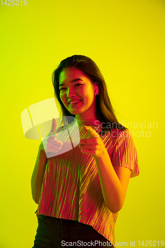 Image of Beautiful girl\'s facial expression in neon light on yellow studio background