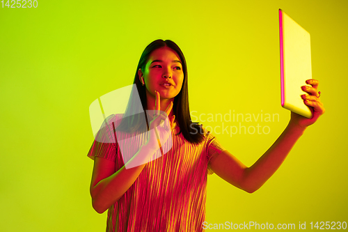 Image of Beautiful girl\'s facial expression in neon light on yellow studio background