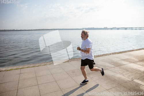 Image of Senior man as runner with armband or fitness tracker at the riverside