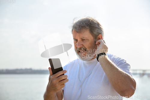 Image of Senior man as runner with armband or fitness tracker at the riverside