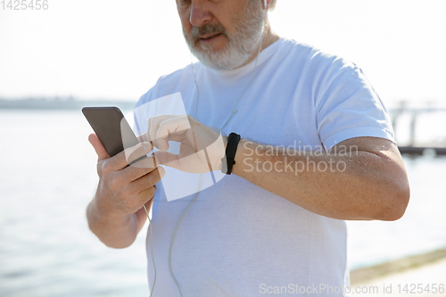 Image of Senior man as runner with armband or fitness tracker at the riverside