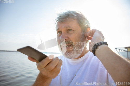 Image of Senior man as runner with armband or fitness tracker at the riverside