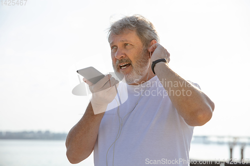 Image of Senior man as runner with armband or fitness tracker at the riverside