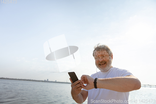 Image of Senior man as runner with armband or fitness tracker at the riverside