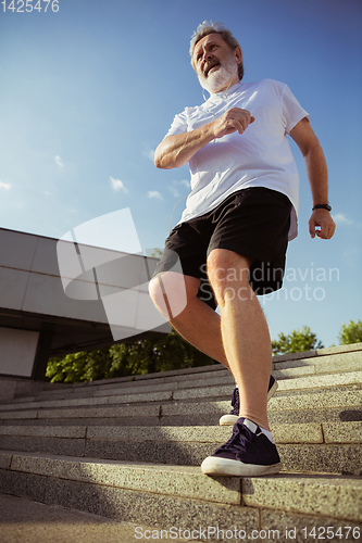 Image of Senior man as runner with armband or fitness tracker at the city\'s street