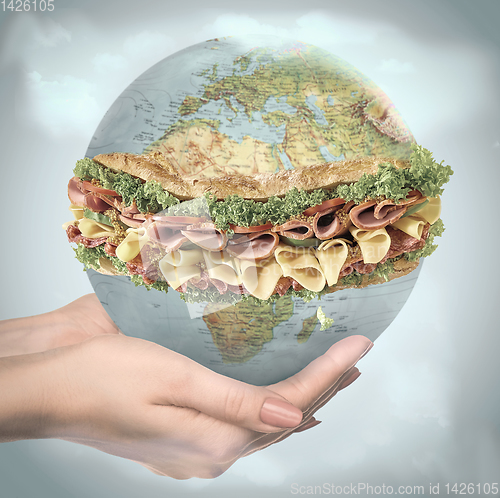 Image of Save healthy food - female hands holding a globe as a sandwich