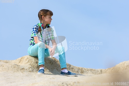 Image of A teenage girl crouched on the top of a mountain and resting examines the surroundings