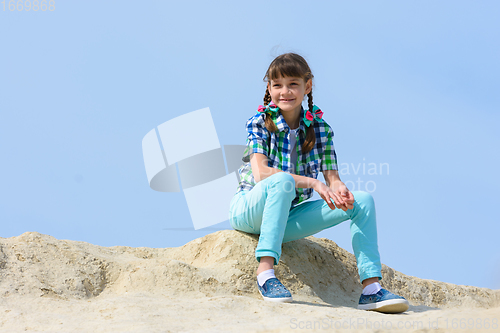 Image of A ten year old girl sits on a hilltop and smiles