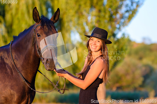 Image of Happy girl in a hat and a horse in the rays of the warm setting sun looked into the frame