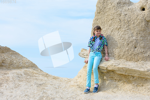 Image of A ten-year-old girl sat down on a rock ledge resting after climbing