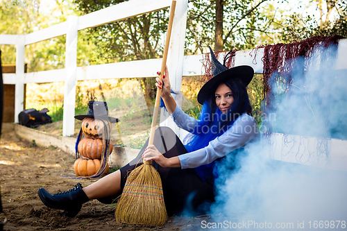 Image of A girl dressed as a witch sits by the fence, thick white smoke creeps out from behind the fence