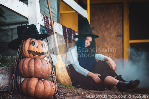 Image of In the foreground there is a figure of pumpkins with a vicious face, in the background a witch sits