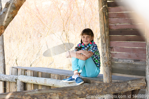 Image of A ten-year-old girl sits in a wooden gazebo and looks cheerfully into the frame