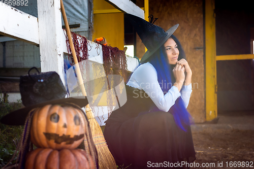 Image of In the foreground there is a figure of pumpkins with a vicious face, in the background a witch sits dreamily