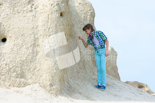 Image of A girl of ten years old picks her finger in the rock with interest