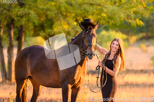 Image of The girl put a hat on the horse for a walk and happily looked into the frame, portrait