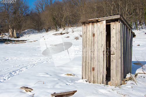 Image of An old wooden street toilet stands alone on an empty snow-covered plot