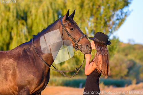 Image of A girl kisses a horse in the rays of the setting sun