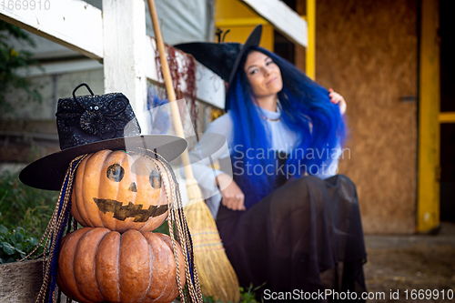 Image of In the foreground is a figurine of pumpkins, in the background a witch sits by the fence