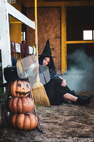 Image of A girl dressed as a witch with a broom squatted by the fence at the Halloween celebration