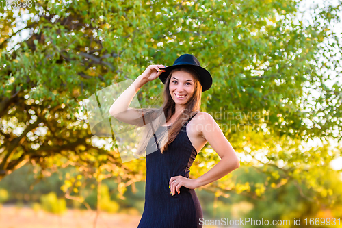 Image of Portrait of a beautiful girl on a background of blurry foliage, the girl holds a hat with one hand