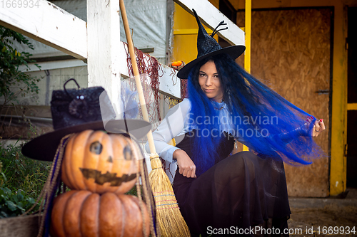 Image of A witch with blue hair sits by the fence next to an evil pumpkin figure