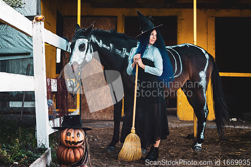 Image of A girl dressed as a witch stands by a corral on a farm next to a horse