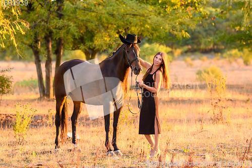 Image of The girl put a hat on the horse for a walk and happily looked into the frame