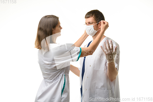 Image of The nurse puts a medical mask on the doctor\'s face