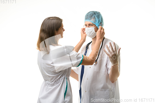 Image of Nurse putting medical mask on surgeon face isolated on white
