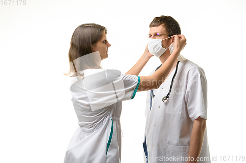 Image of The nurse puts a medical mask on the doctor\'s face with glasses
