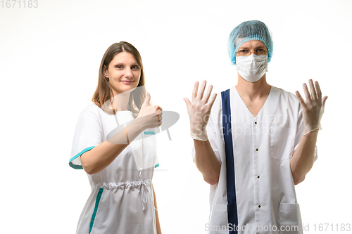 Image of A nurse stands next to a doctor in a medical mask, a cap and sterile gloves and happily points up